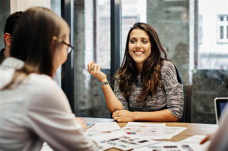 A group of professionals having a discussion in a modern office setting with charts and documents spread on the table..