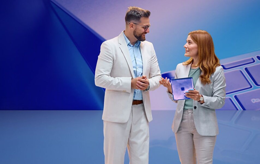 Ein Mann und eine Frau unterhalten sich, die Frau hält ein Tablet. Im Hintergrund ist eine Tastatur zu sehen.