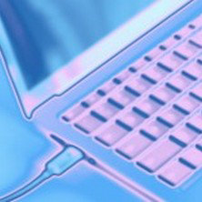 「キーボードと画面の一部が見えるノートパソコンを斜めからとらえた青みがかった描写。電源ケーブルが接続されている様子が確認できる。」