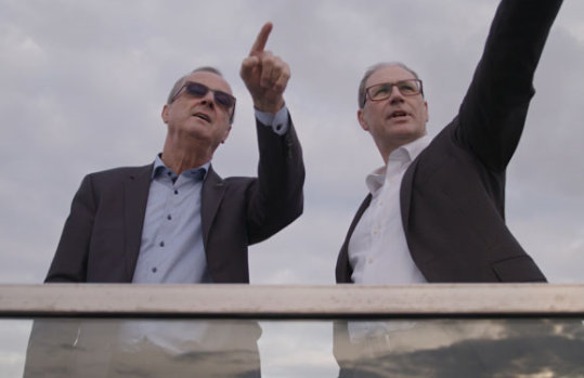 Zwei Männer auf dem Dach eines Haus zeigen Richtung Horizont