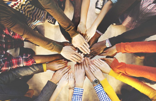 Menschen stehen im Kreis und haben ihre Hände im Zentrum des Kreises aufeinander gelegt.