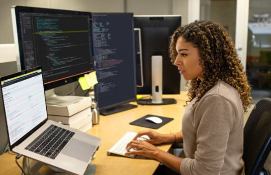 Frau sitzt an Schreibtisch mit mehreren Bildschirmen