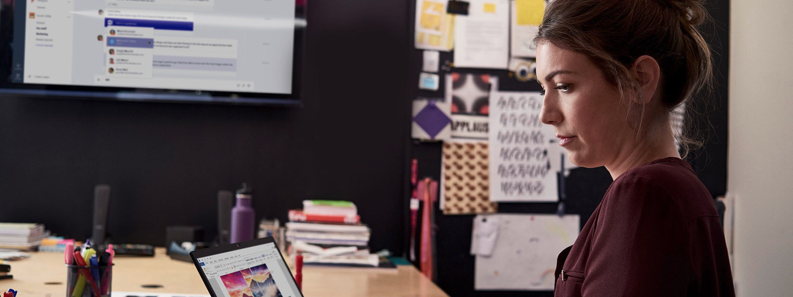 Frau sitzt an modernem Arbeitsplatz am Laptop, ein weiterer Screen ist im Hintergrund zu sehen