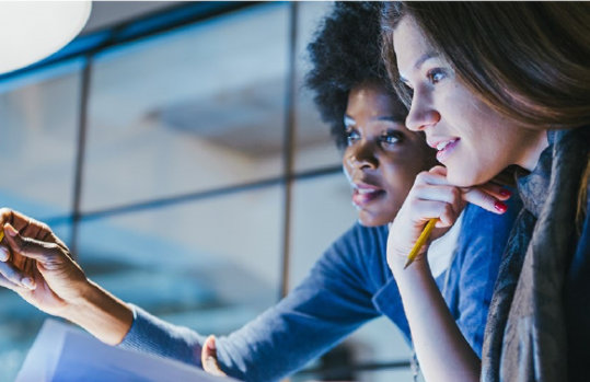 Zwei Frauen, die an einem aufgeklappten Bildschirm etwas besprechen