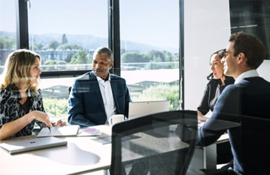 Zwei Frauen und zwei Männer sitzen an einem Konferenztisch in einem hellen Konferenzraum