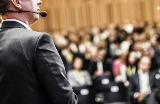 Sprecher im Anzug, der vor einem Publikum steht