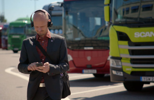 Ein Mann mit Kopfhörern geht an einem Scania-Lastwagen vorbei, der im Hintergrund steht.