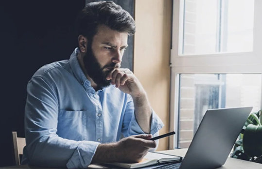 Ein Mann sitzt an einem Tisch und arbeitet an seinem Laptop