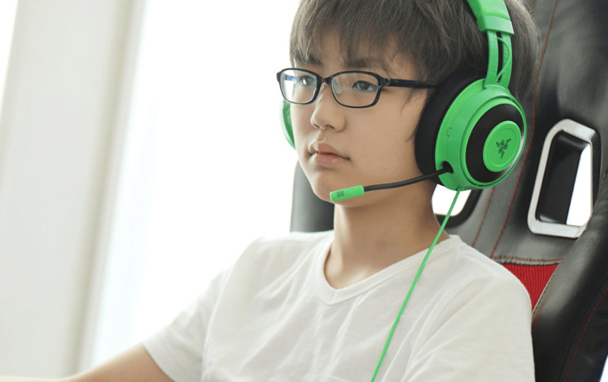 男の子は緑色のヘッドフォンを着用し、コンピューターでゲームをしています。