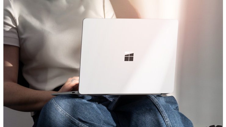 膝の上でプラチナカラーの Surface Laptop を操作している​