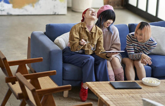 ソファに座ってタブレットPCを見て笑っている 3 人の女性