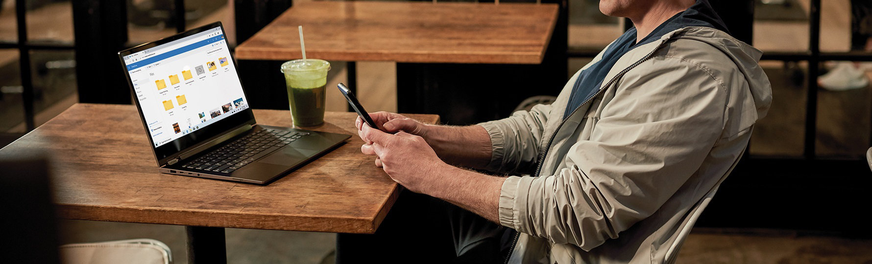 カフェでテーブルの上にノート PC を置き、スマートフォンを操作する男性
