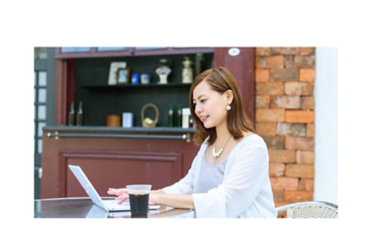 カフェでコーヒーグラスを持ってノートパソコンで作業する女性