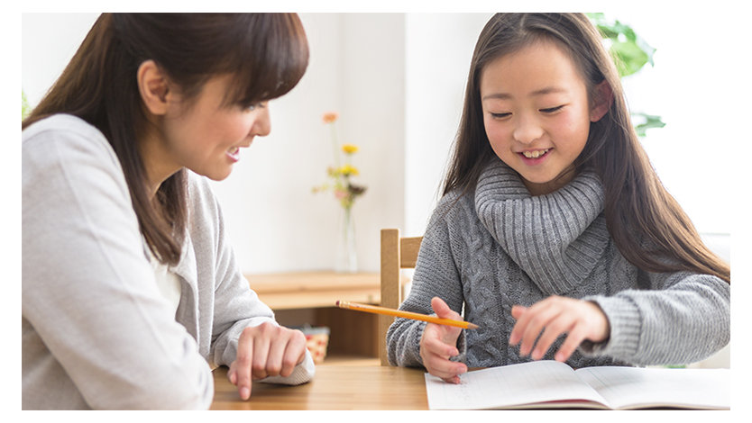 ノートに向かう女性と鉛筆を持つ女の子が、一緒に微笑んでいる様子