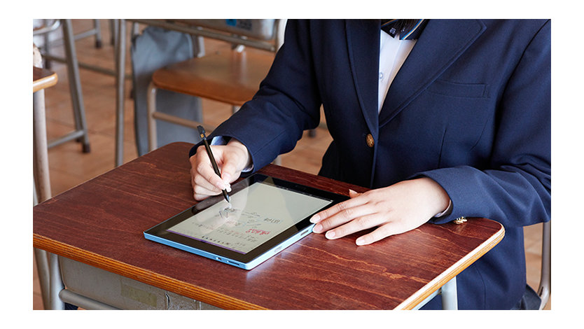 教室の机でタブレットモードのノート PC にペンで入力する高校生