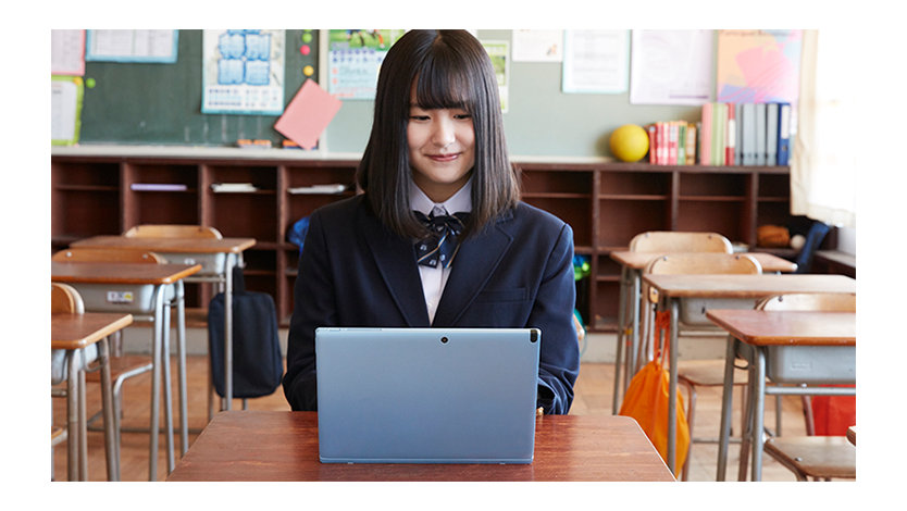 教室の机でノート PC を操作する高校生