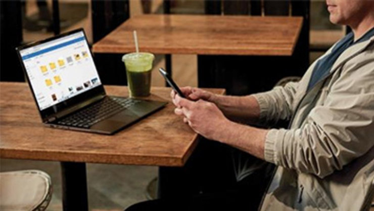 カフェでテーブルの上にノート PC を置き、スマートフォンを操作する男性