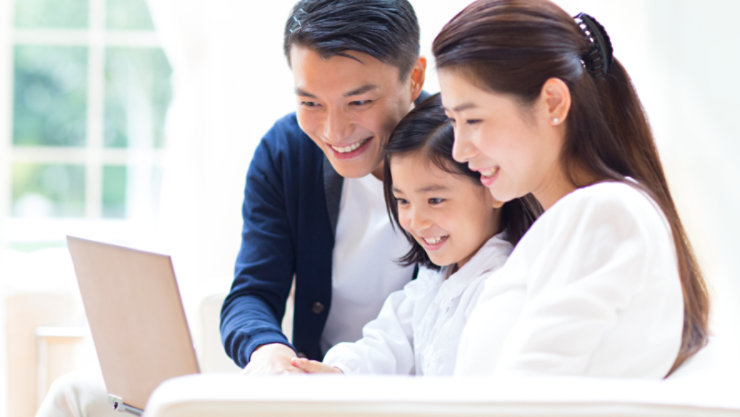 小さな女の子とその父親と母親がノートパソコンの画面を見て微笑んでいる