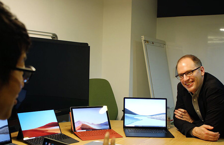 4 台の Surface ラップトップをテーブルに置き、Surface ラップトップについて説明する男性