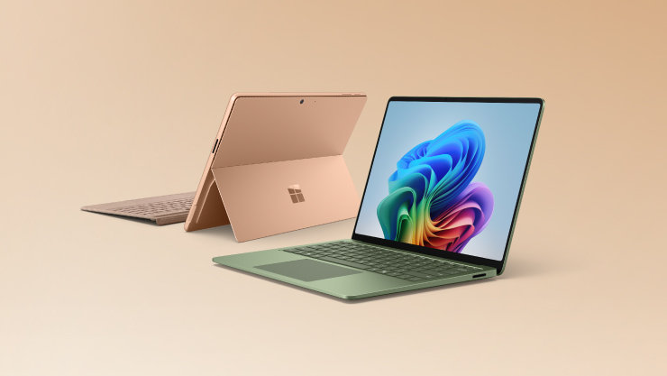ベージュの背景に並ぶ2台のMicrosoft Surface。手前にはカラフルな抽象デザインの画面が表示された薄緑色のノートPC、奥にはMicrosoftの4つの四角形ロゴが背面に見えるローズゴールドのタブレットとキーボード。