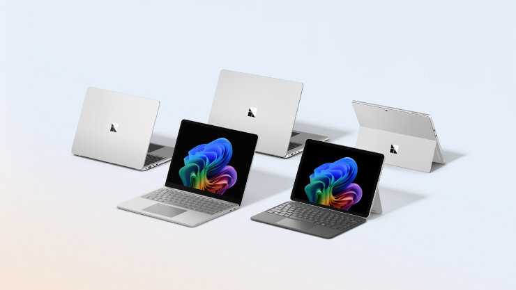 明るいブルーの背景に並ぶ5台のシルバーのMicrosoft Surface。手前には鮮やかな抽象デザインの画面が表示されたノートPCとキーボード付きタブレット。
