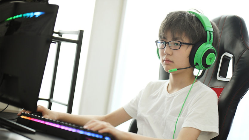 男の子は緑色のヘッドフォンを着用し、コンピューターでゲームをしています。