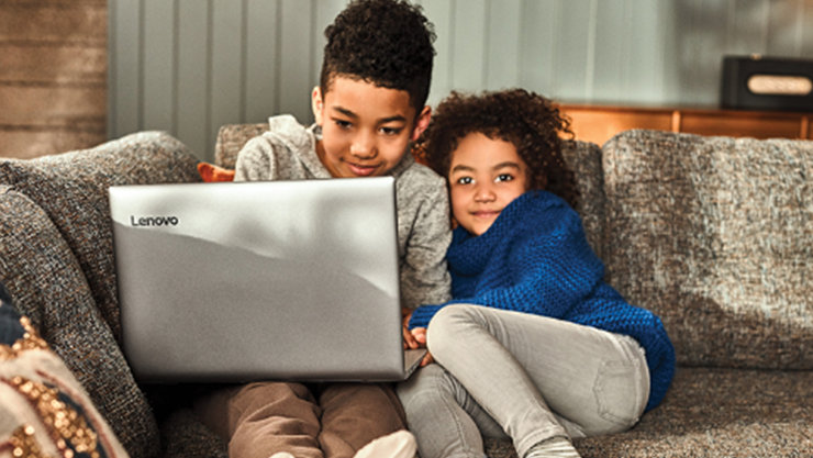 Zwei Kinder sitzen auf einem Sofa, ein Kind bedient einen Laptop