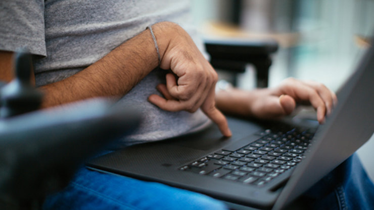 Gezeigt wird eine sitzende Person von der Brust bis zu den Knien, sie bedient einen Laptop, der sich in ihrem Schoß befindet