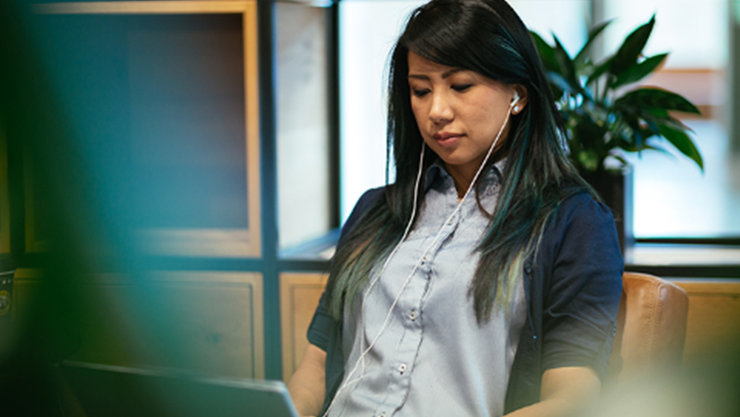 Eine Frau sitzt auf einem Stuhl und bedient einen Laptop, während sie In-Ear-Kopfhörer verwendet