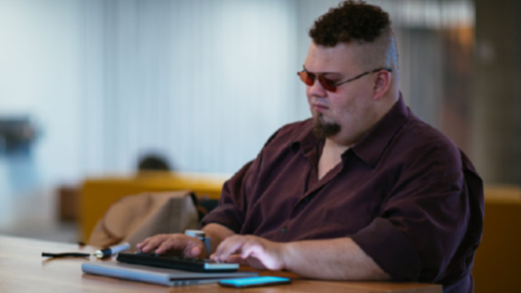 Ein Mann sitzt an einem Schreibtisch und verwendet unterstützende Technologien