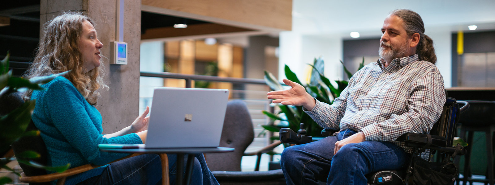 Ein Mann, der in einem Rollstuhl sitzt, redet mit einer Frau am Laptop.