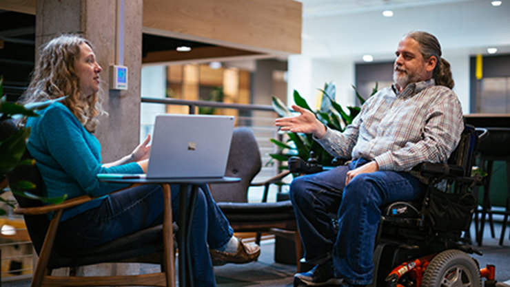 Ein Mann, der in einem Rollstuhl sitzt, redet mit einer Frau in einem Büro