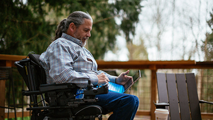 Eine Person in einem Rollstuhl sieht sich Inhalte auf einem Laptop an, während sie sich draußen auf einer Terrasse befindet