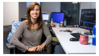  縞模様のトップスを着た女性が机に座って微笑んでいる