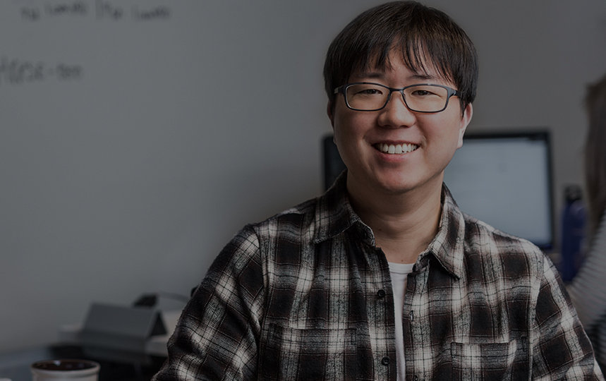 チェック柄のシャツを着た男性が座って微笑んでいる