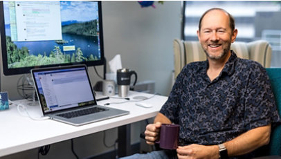 机に座り、コーヒーマグを手にした男性開発者