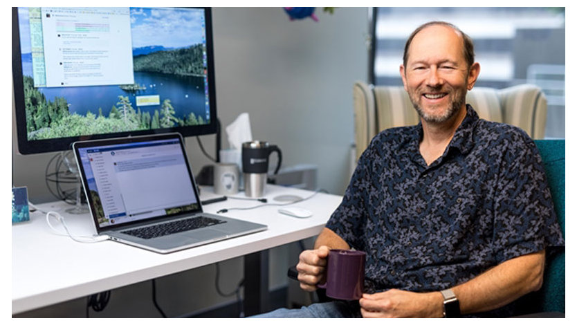 机に座り、コーヒーマグを手にした男性開発者