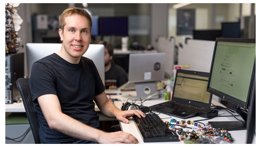 机の上に座っている男性開発者は、ラップトップ、モニター、キーボード、カラフルなビーズを持っています