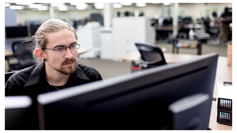 青いヘッドフォンを着けて机に座る男性開発者