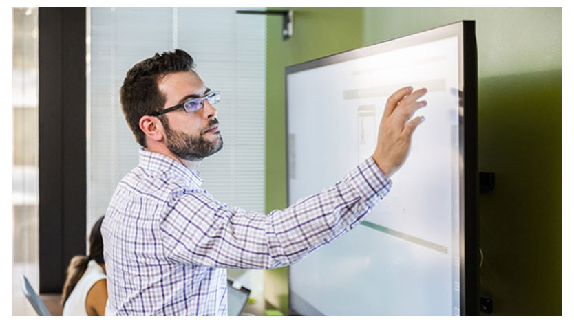  壁の大きなモニターの近くに眼鏡をかけた男性