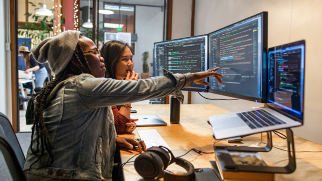 女性開発者がコンピュータ上のコードを同僚に見せている