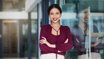 自信を持って若いビジネスウーマンが笑顔でガラスの壁のそばに立つ