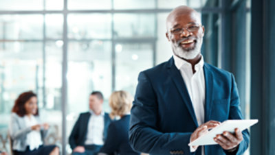 現代のオフィスでデジタルタブレットを使用し、同僚を背景にしている成熟したビジネスマン