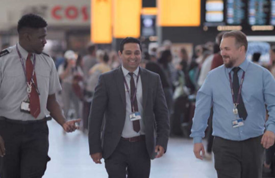 3 人の空港職員が談笑しながら並んで歩く様子