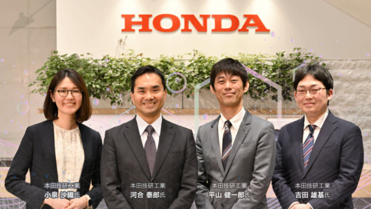 「HONDA」のロゴと植物を背景に、4人のビジネスパーソンが立っている。