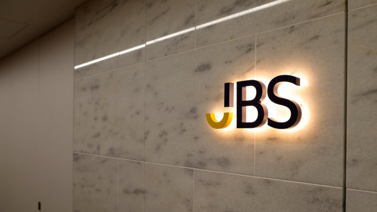 壁に設置された、背後から光る「JBS」のロゴ。ロゴの「J」は黄色で、「BS」は黒色。