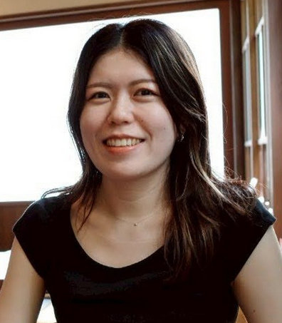 清水 美佳氏が、自然光の入る窓の近くの室内で黒いトップスを着て座っている。