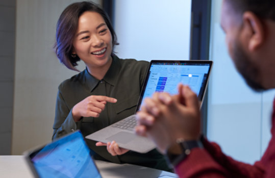 Surfaceラップトップで統計を提示する笑顔の女性。