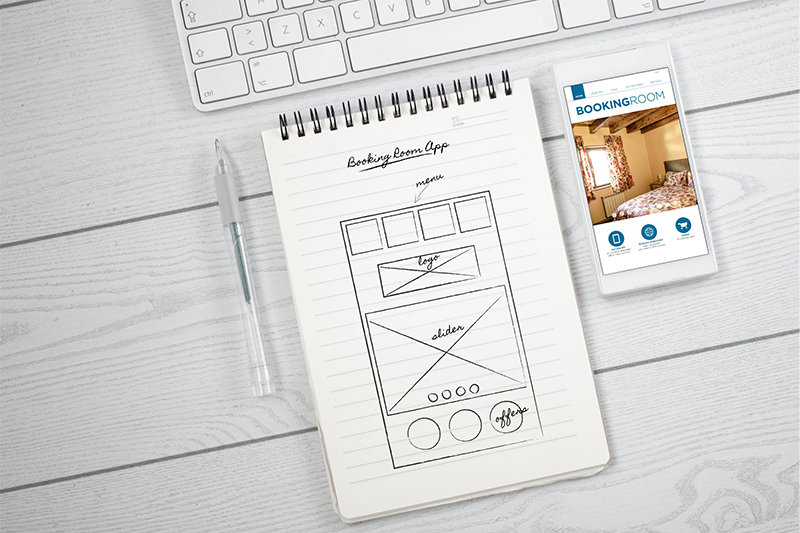 ノートに書いたアプリの画面イメージと横に置かれたスマートフォン