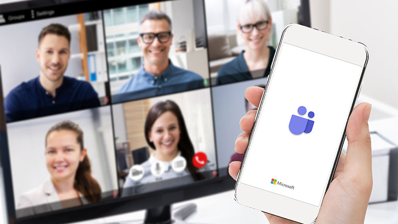 Web 会議参加者が表示されたディスプレイと Microsoft Teams のアイコンが表示されたスマートフォン